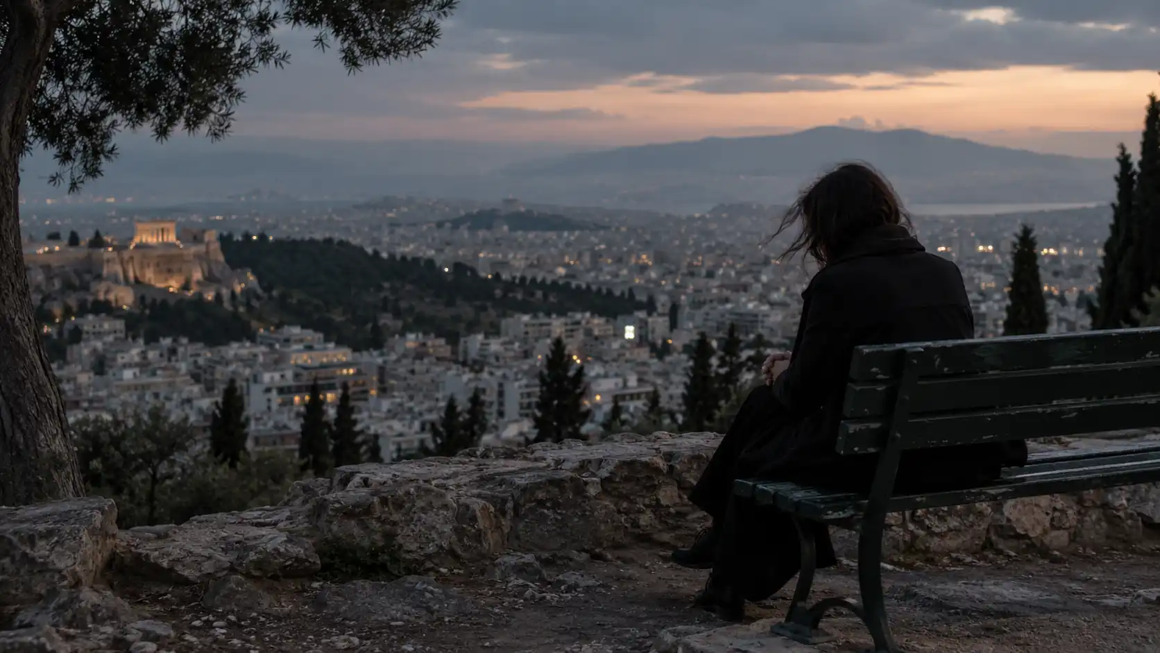 Άτομο καθισμένο σε παγκάκι με θέα την Αθήνα στο σούρουπο
